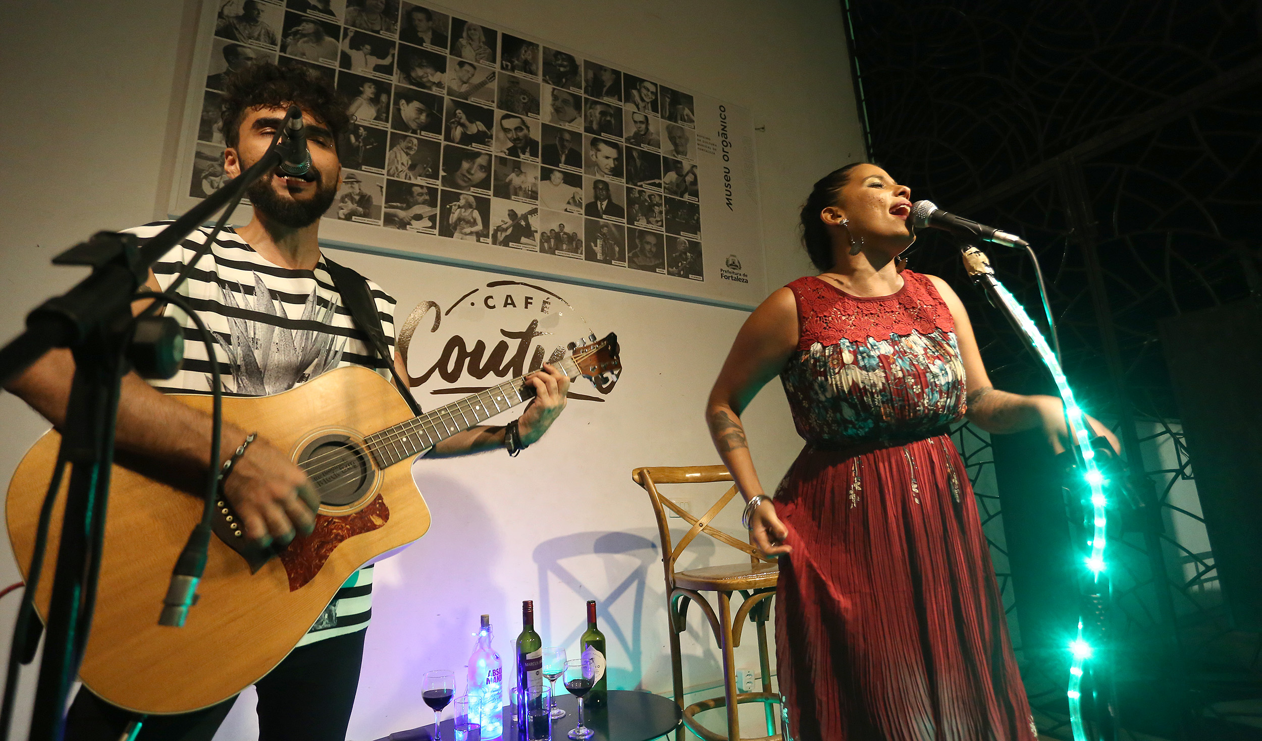 Nayra Costa cantando num palco ao lado de um músico com violão